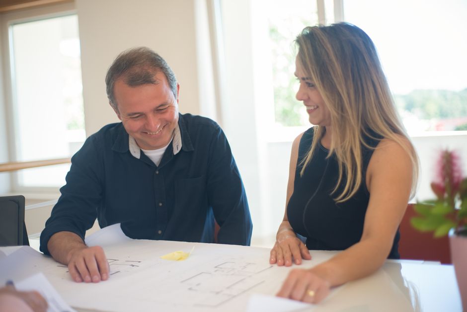 A smiling couple reviews real estate plans together in a bright indoor setting.